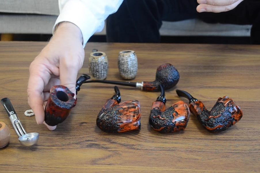 A person displaying various carved smoking pipes on a wooden table.